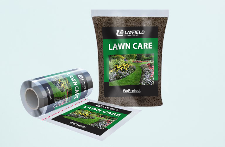 Packaging design for ‘LAWN CARE’ by LAYFIELD with the tagline ‘WeProtect’. The packaging features a vibrant garden with lush green grass and colorful flowers. A roll of the packaging material and an unfolded flat version showcasing the same design elements are also visible.